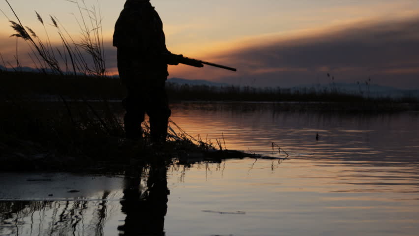 silhouette of a duck hunter standing on the lake