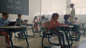 Young schoolteacher talking with pupils in classroom. Female teacher explaining lesson to mixed race students. Focused schoolchildren using digital tablets in school class. Kids doing class work  - Powered by Shutterstock - Get 15% off with code: PIKWIZARD15