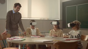 Smiling teacher having interactive lesson with pupils in 3d vr glasses in classroom. Happy classmates playing video games in virtual reality headsets. Positive kids and male teacher having fun 