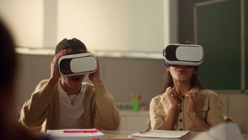 Excited kids in vr glasses learning in modern school. Positive classmates wearing virtual reality headsets during interactive lesson in classroom. Mixed race children immersing in virtual reality | Shutterstock HD Video #1075580594