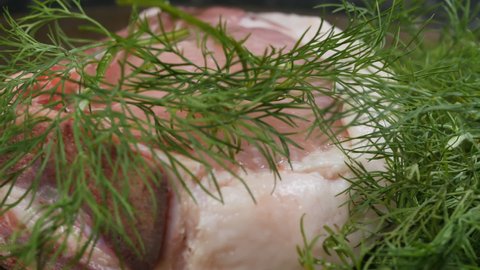 over close-up a piece of fresh pork meat in green dill rotates. Pork entrecote for frying.