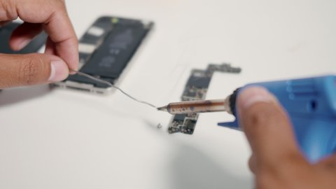 Technician man service repairing inside smartphone motherboard by soldering in the lab to fix mobile phone problem