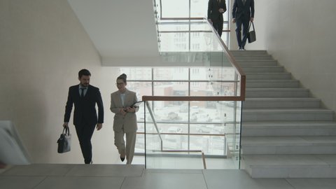 Groups of male and female business people or lawyers having conversation while walking up and down stairs in contemporary office