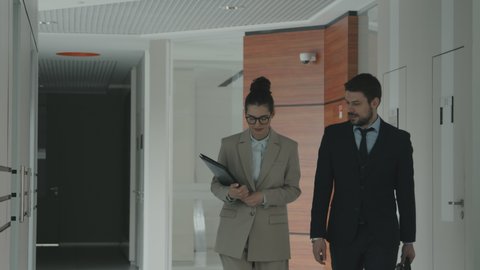 Medium slowmo of couple of successful young lawyers in formalwear talking about work while walking through modern office