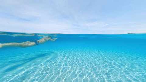 Split-shot, stunning view of a tourist swimming on a beautiful and turquoise water. Caprera, La Maddalena Archipelago, Sardinia, Italy. Over-under shot, half underwater, half sky.