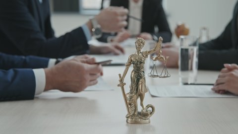 PAN close-up of gold statue of Femida – Goddess of Justice – with scales at lawyers conference table during their meeting