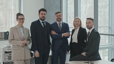 PAN medium slowmo portrait of successful team of lawyers in formalwear posing for camera standing together in modern office room