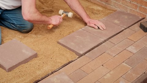 Worker lays tiles on the pressed sand. Slow motion view