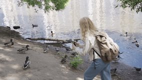 A woman tourist with a large backpack is filming ducks on a pond. Travel and active life concept.
