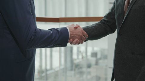 Midsection slowmo of unrecognizable lawyers or business partners in suits shaking hands in office making deal