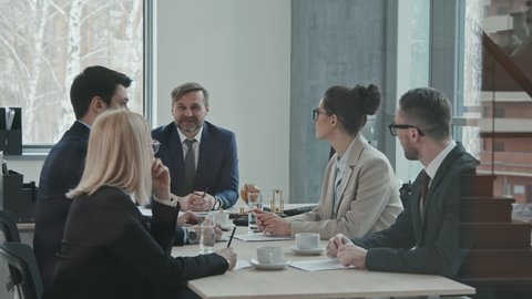 Medium PAN slowmo of mature male executive of law company having meeting with colleagues discussing legal matters at conference table
