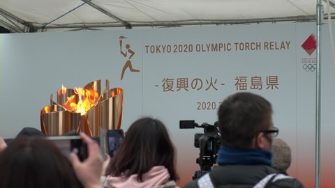 FUKUSHIMA, JAPAN - 24 MARCH 2020 : Olympic Flame displayed at Fukushima station. Tokyo Olympic 2020 have been postponed to 2021 due to coronavirus. Crowd of people wearing surgical masks.
