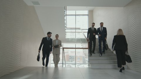 Successful male and female lawyers in formalwear walking up and down stairwell in modern office