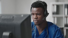 Afro-american male doctor or nurse with headset and computer working at hospital .young professional therapist doctor consulting customer client using remote communication speaking on webcam