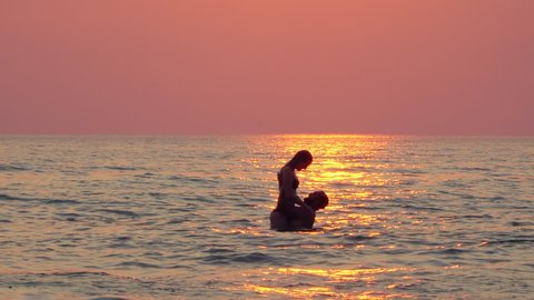 Couple in love having romantic tender moments, kissing and hugging at sunset in the sea. Honeymoon and romantic vacation concept