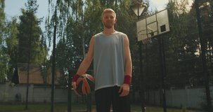 Male basketball player confident young athletic guy with ball posing standing on basketball court outdoors
