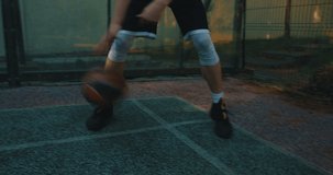 Male basketball player dribbling ball between legs, scoring hoop during training on basketball court