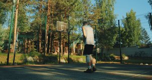 Basketball player scoring a ball in hoop on basketball court outdoors in summer. Slow motion