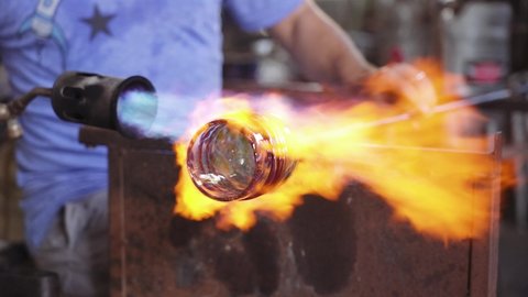 A glass blower heating a whiskey glass with fire flames.