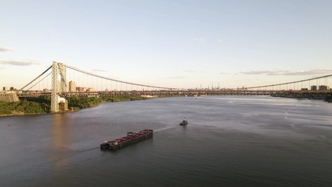 Industrial barge traveling up Hudson River toward New York City skyline at golden hour