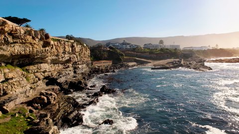 Hermanus Old Harbour and textured cliffs, balmy weather during sunrise with waves gently crashing into rocky coastline
