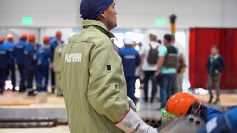 Sochi, Russia - August 07 2019: Caucasian people workers wear special uniforms, work suits, protective orange hard hat, glasses, stand in factory room close up. Start of working day concept.