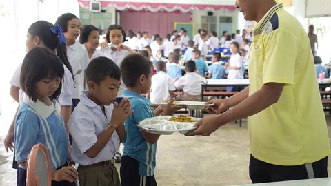 Yala, Thailand Nov 17, 2015: Lunch time Thai primary students in the canteen boys and girls in uniform  receiving plate with food from teacher Thesaban School