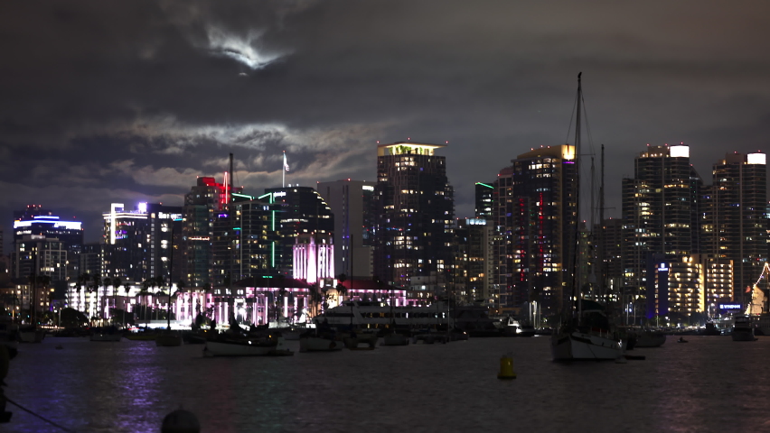 Timelapse of the skyline in San Diego at night as clouds block the full moon in the sky.