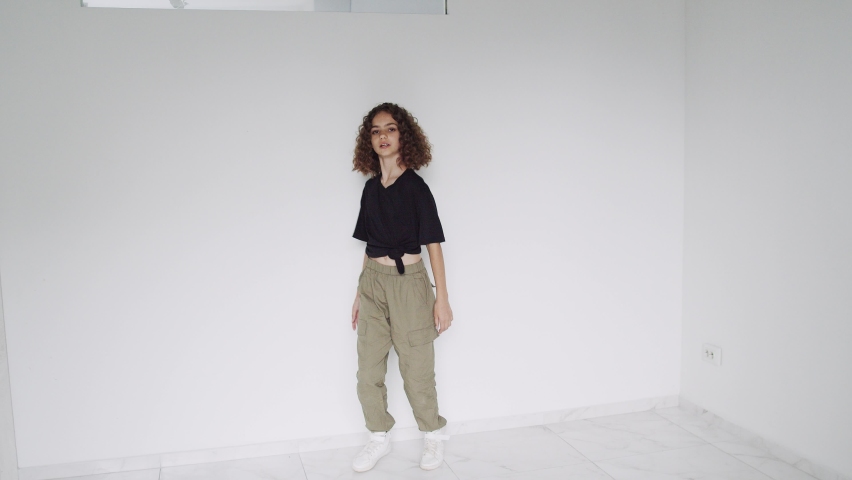Young lady dances, making slow moves on white background