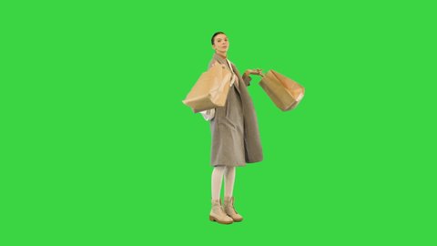 Young girl in stylish clothes dances slightly with paper bags in hands on a Green Screen, Chroma Key.