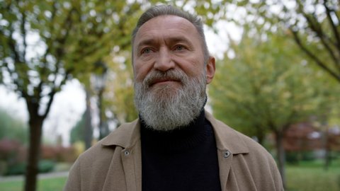 Portrait of mature man with long grey beard outdoors. Old man going meet someone on autumn day. Close up of caucasian good looking senior going in fall park outside.