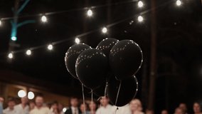 Bunch of black balloons background of glowing garland of light bulbs and silhouettes of people at night. Dart flies, balloon explodes and blue confetti flies out of it, people applaud. Gender party. - Powered by Shutterstock - Get 15% off with code: PIKWIZARD15