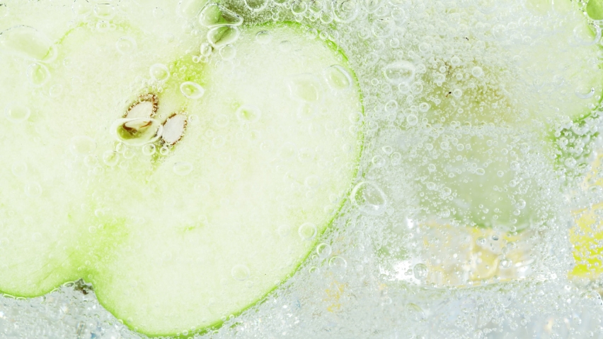 Super Slow Motion Shot of Fizzing Water with Apple Slices and Ice Cubes in Glass at 1000 fps.