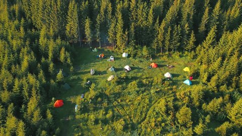 Flight over a tent camping group of tourists in the mountains at sunrise. Potato town of a group of climbers from a bird's eye view. Tourist camp in the green forest