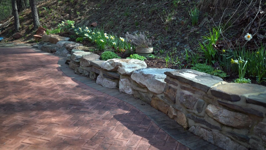 Slow slider to the right brick pavers, rock wall, garden with hill and forest.