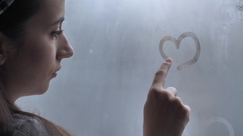 Young woman drawing a heart on a window