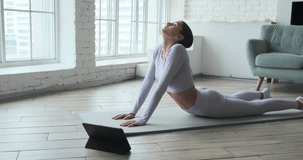 Young happy woman practicing yoga and doing breathing exercises watching live video learning classes on tablet. brunette enjoying fitness pilates workout alone at home. Healthy and balanced lifestyle.