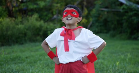Happy asian little hero boy in red laugh in a beautiful garden. Boy dressed as a super hero in a park. Superhero kid against in the garden. Boy power concept. Happiness and love for children concept.