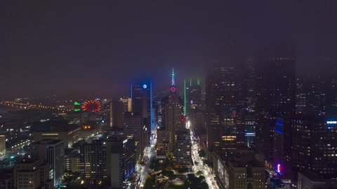Evening hyper lapse footage of high skyscrapers in business district, Dallas, USA. View from drone flying towards big neon clock on top of building in 2021