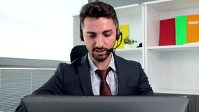 Caucasian young man in suit wearing headphones with mic having video chat at laptop computer in call center. Holding online negotiations, consultation, meeting or business conference. 