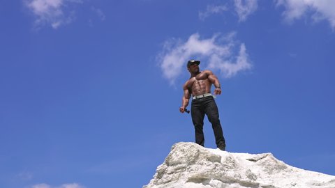 Bare torso of black skinned athlete. African american bodybuilder on the top of white hill against blue sky background. View from below.