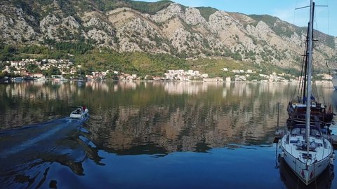 Kotor, Montenegro - September 2019: White motor boat sailing in morning from Kotor Boko bay Montenegro with moored luxury white yachts, sailing boats, cruise Tui ship docked in the Adriatic Sea