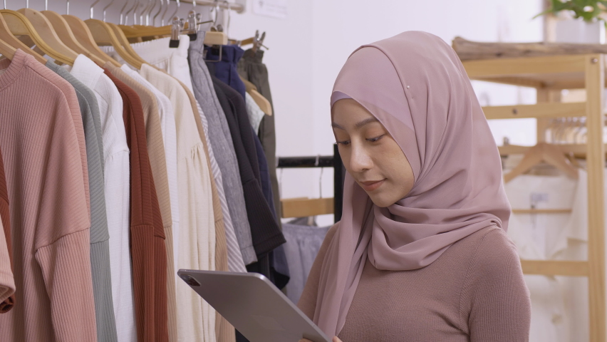 Young muslim woman checking her product stock at her shop. She using tablet to work.