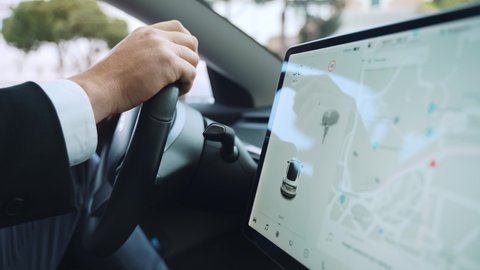 Side view of person's hands holding steering wheel while driving a car on the street road, businessman using touch screen monitor for navigation apps and other online functions. Driver's hands on car