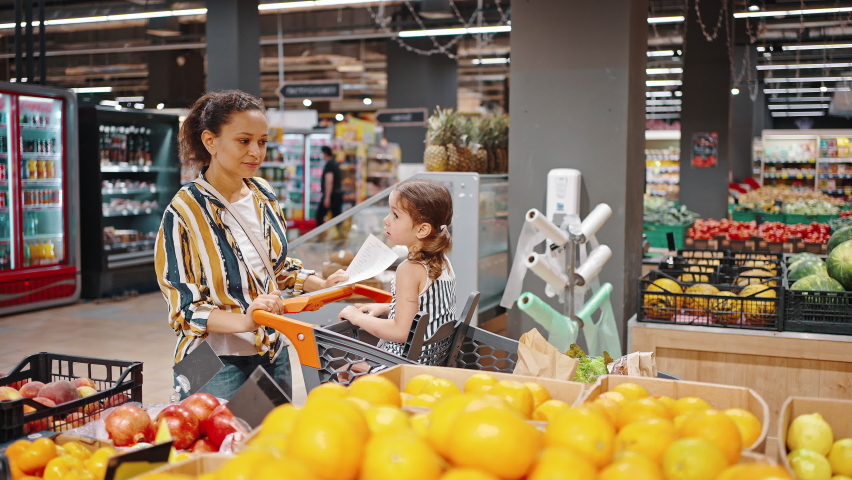 Lovely family, mother and little daughter buy lemons in the hypermarket in the fruit section. Girl sitting in a supermarket trolley. Vegetarianism and healthy food concept. Royalty-Free Stock Footage #1075702790