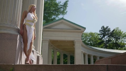 sexy blonde lady is dressed ancient greek gown, posing near column of old palace