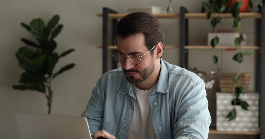 Focused young man freelancer in eyeglasses working on computer at home office, looking in distance searching for inspiration, creating online project, thinking on problem solution, typing email. Royalty-Free Stock Footage #1075713062