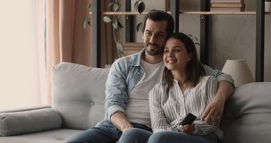 Affectionate bonding loving happy young married couple resting on comfortable sofa, watching interesting smart TV channels programs, choosing comedian movie, enjoying romantic relaxed family time.