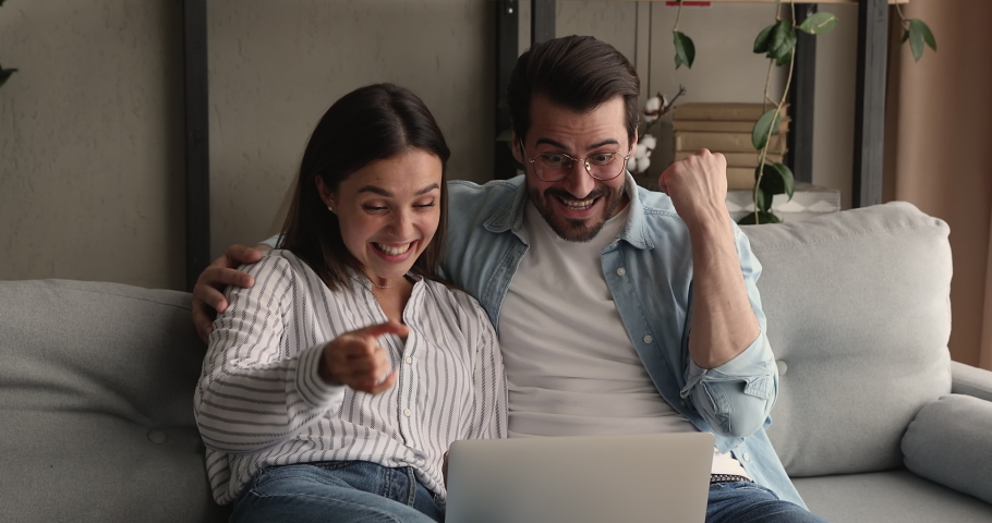 Bonding happy young family couple looking at laptop screen, reading email with amazing news, celebrating winning online lottery or giveaway, getting bank loan mortgage approvement, victory concept. | Shutterstock HD Video #1075713170