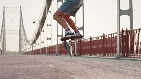Close-up of a girl's leg performing complex tricks on a skateboard on the city bridge. Jump and flip. Group of skaters, boys and girls, ride their skateboards.